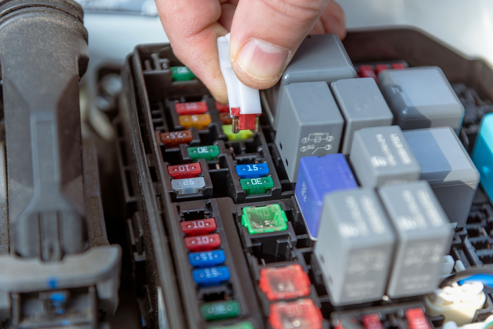 Car mechanic hand checking a fuse in a car engine